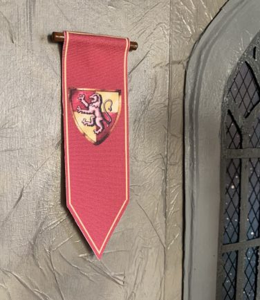A completed red and yellow miniature Gryffindor House Banner on a wall of the Great Hall room of a Hogwarts Castle Dollhouse. 