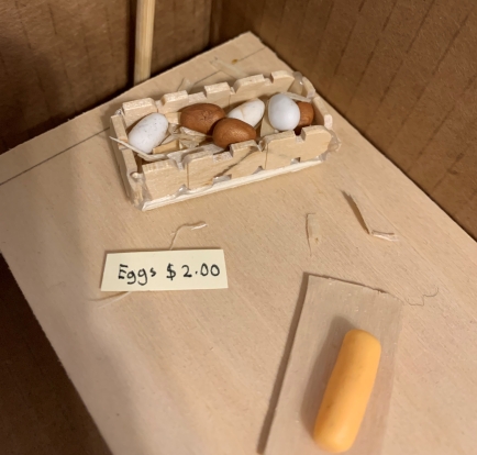 A miniature wooden crate filled with straw, with a few brown and white eggs nestled on top.